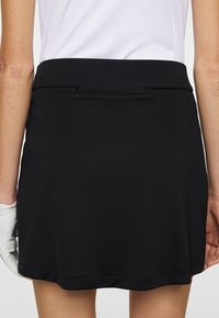 Svart golfkjol med platt midjeband, mjuk textur och en subtil kanten. Designad för komfort och prestanda under spelet.