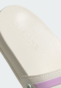 Adidas slide sandal in white, featuring a textured upper, contrasting lavender stripe, and embossed logo. Smooth, curved design.