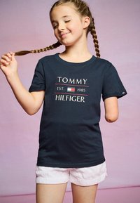 Námořnické bavlněné tričko s bílým a červeným logem "TOMMY HILFIGER", krátkými rukávy a volným střihem, spárované se světle růžovými šortkami.