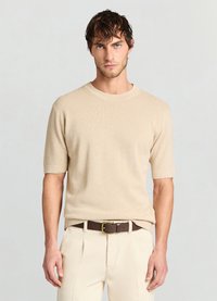 Pull beige en maille à manches courtes avec un col rond, motif texturé, porté avec un pantalon de couleur claire et une ceinture marron.