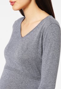 Grauer, langärmliger Pullover mit V-Ausschnitt, aus weichem Strickmaterial gefertigt. Verfügt über eine leicht taillierte Form und dezente Rippendetails.