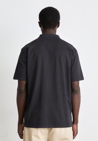 Tricou polo negru cu mânecă scurtă dintr-un material texturat. Acesta are un guler clasic și o margine dreaptă. Spatele este simplu, fără embellisuri.