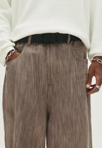 Pantaloni texturați de culoare maronie cu un design drept, având buzunare frontale și o curea neagră, completate de un top alb din tricot cu model waffle.