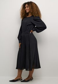 Musthaveeritud must midi kleit, millel on pikad puffvarrukad, elastne vöökoht, sile kangas ja õrn sära. Kandmiseks punase varbaga sosside kõrgele kontsaga.