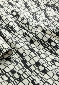 Tessuto nero e bianco sporco con un motivo geometrico di rettangoli e linee, caratterizzato da una texture liscia e un design leggero.
