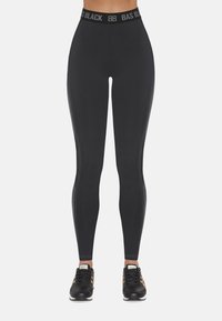 Czarne legginsy z szerokim elastycznym paskiem w talii z logo "BAS BLACK". Gładka tekstura z detalami bocznych paneli. Połączone z czarnymi butami sportowymi.
