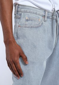 Jasnoniebieskie dżinsy z pięcioma kieszeniami, kontrastowym szwem i zamkiem błyskawicznym. Gładka tekstura, luźny krój i lekko zwężana nogawka.