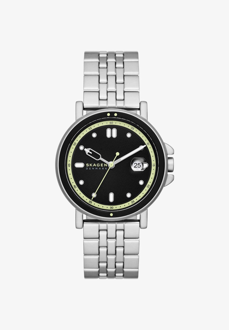 Skagen-rannekello mustalla kellotaululla, hopeisilla osoittimilla, päivämääränäyttö kello kolmessa, hehkuvilla viisarilla ja hopeisella metallirannekkeella.