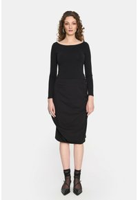 Czarna bluzka z długim rękawem w połączeniu z czarną spódnicą ołówkową, charakteryzującą się gładką fakturą, dopasowanym krojem i długością do połowy łydki. Czarne skarpetki do kostek i buty.