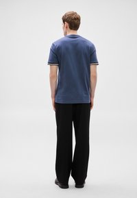 Tengeri kék pamut rövid ujjú póló kontrasztos csíkos mandzsettákkal, széles fekete nadrággal párosítva. Hátulnézet.