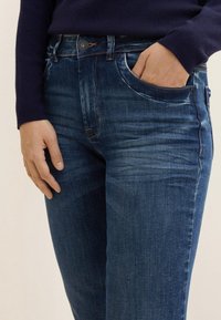 Tmavě modré džíny s úzkým střihem, které mají jemné žmolkování, design s pěti kapsami a mosazné zapínání v pase.