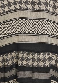 Vävd tyg med växlande svarta och beige mönster, inklusive hundtand och zigzag, som skapar distinkta texturerade band.