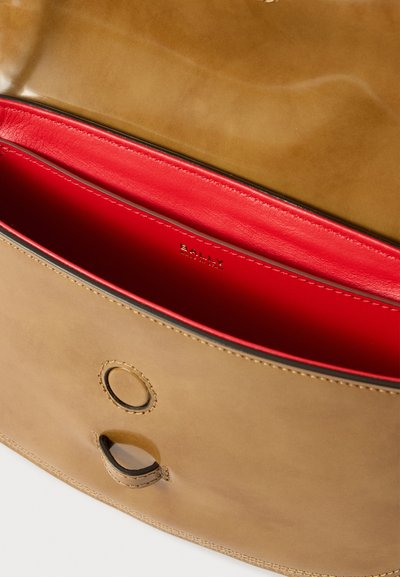 Sac en cuir avec un extérieur en cuir brillant couleur noisette, un intérieur rouge et une découpe circulaire à l'avant. Présente des coutures précises et une étiquette de marque visible.