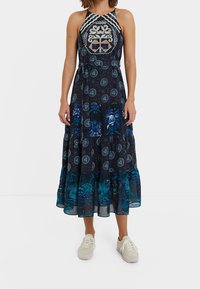 Maxikleid mit einem Halterneck-Design, auf dunklem Hintergrund mit komplexen Stickmustern in Blau und Weiß, featuring einem gestuften Rock und floralen Akzenten.