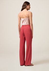 Jasnoróżowa satynowa koszulka na ramiączkach z regulowanymi ramiączkami, w połączeniu z wysokim stanem, szerokimi spodniami w kolorze koralowym, z marszczonym paskiem w talii.