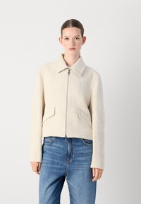 Crème-kleurige cropped jas met een textuurafwerking, een kraag en ritssluiting. Heeft twee voorzakken en lange mouwen.