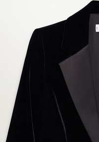 Czarna aksamitna marynarka z satynowymi klapami, charakteryzująca się strukturalnym fasonem i gładką teksturą. Zbliżenie ukazuje eleganckie wykończenie kurtki.