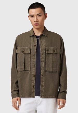 Chaqueta de camisa color verde olivo hecha de tela ligera, con dos grandes bolsillos en el pecho, cierre de botones y cuello clásico.