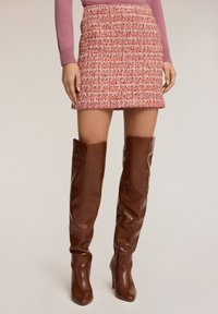 Červená mini sukně z tweedu s texturovan�ým povrchem, v kombinaci s vysokými hnědými koženými botami. Sukně má přiléhavý střih a pasový lem.