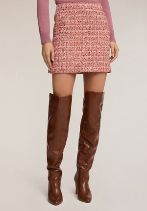 Czerwona mini spódniczka z tweedu o teksturowanym wykończeniu, w połączeniu z wysokimi brązowymi skórzanymi kozakiem. Spódniczka ma dopasowany krój i pasek. 