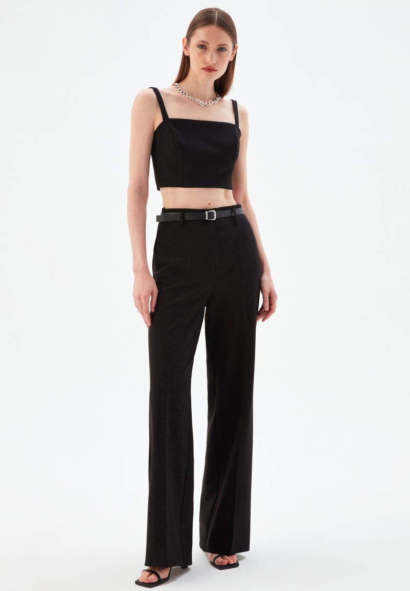 Top negro corto con escote cuadrado, pantalones de pierna ancha y un cinturón negro. Collar de cadena de plata gruesa, textura de tela suave.