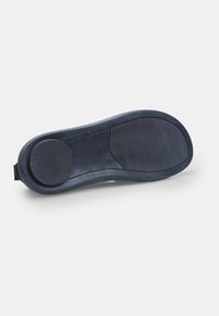Tălpi de sandale din cauciuc negru, arătând zonele texturate de grip pe călcâi și pe minge pentru aderență, izolate pe un fundal alb.