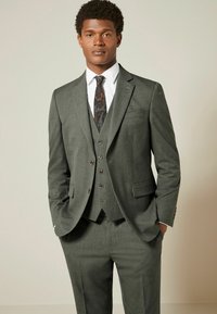Costume gris trois pièces en tissu texturé, comprenant une veste à un bouton, un gilet et une cravate à motifs. Coupe ajustée et chemise assortie.