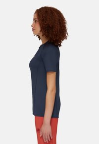 Navyblaues Kurzarmhemd aus weichem, dehnbarem Stoff; hat flache Nähte und eine figurbetonte Silhouette, kombiniert mit leuchtend orangefarbenen Hosen.