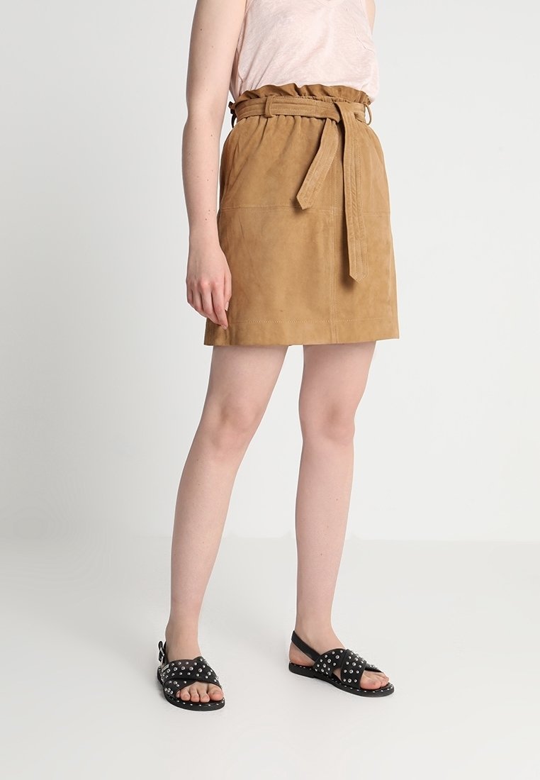 Tan mockasinskjol med bälte i midjan och en figurnära silhuett. Matchad med svarta naggade sandaler. Toppen är ljusrosa med en avslappnad passform.