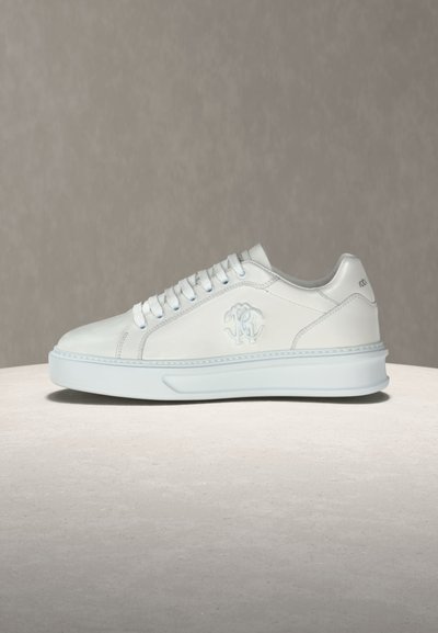 Άσπρο sneaker χαμηλού τύπου με λευκά κορδόνια, ανάγλυφο λογότυπο στο πλάι και πάτο με παχιά επένδυση σε ουδέτερο φόντο.