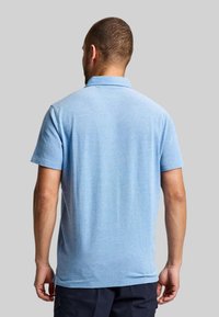 Hellblaues Poloshirt mit kurzen Ärmeln, klassischem Kragen und strukturiertem Stoff, von hinten gezeigt. Einfaches Design, ohne Muster oder Akzente.
