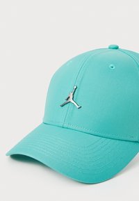 Turkis baseball cap med en tekstureret stof, buet skygge og sølv Jumpman-logo på forsiden. Justerbar lukning bagpå.