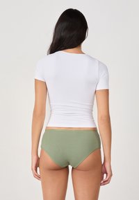 Biała, dopasowana bluzka z krótkim rękawem o gładkiej fakturze, zestawiona z zielonymi, prążkowanymi majtkami o wysokim stanie. Skupienie na widoku z tyłu i kontraście kolorów.