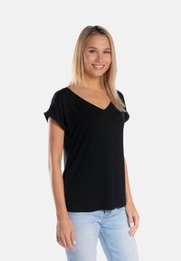 Czarna koszulka z krótkim rękawem w serek, uszyta z mi ękkiego materiału, o lekko luźnym kroju, w połączeniu z jasnoniebieskimi dżinsami.