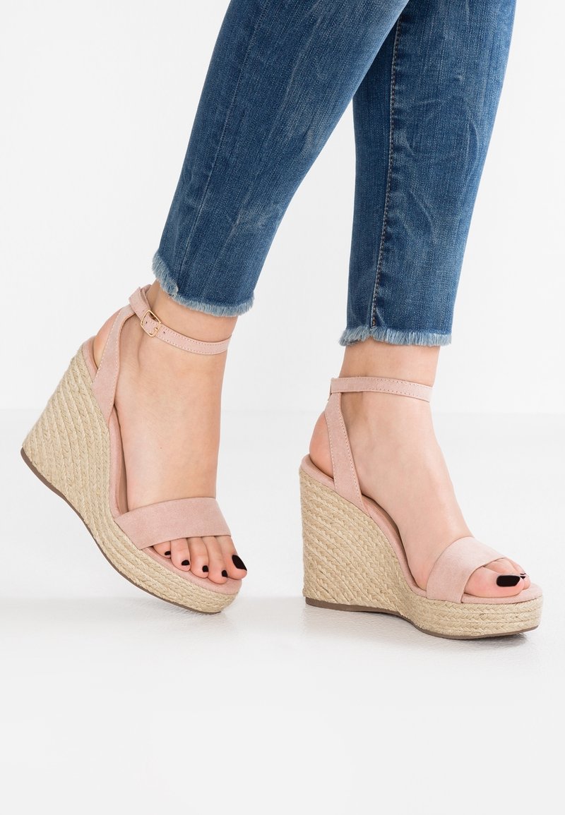 Pieds en sandales compensées rose clair à bride cheville avec semelles plateformes tissées, associées à un jean bleu à ourlet effiloché et un vernis à ongles noir.