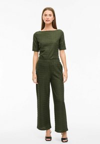 Olijfgroene, gestructureerde jumpsuit met een aansluitende bodice en wijde pijpen. Korte mouwen en een bootnek creëren een ontspannen silhouet.