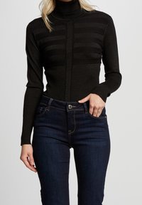 Zwarte coltrui met horizontale geribbelde textuur, slim fit en lange mouwen, gecombineerd met donkerblauwe high-waisted jeans.