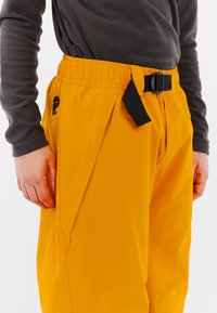 Geel waterdichte broek met een textuurafwerking. Voorzien van een elastische tailleband en een verstelbare zwarte riem. Logo zichtbaar bij de zak.