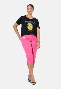 Mustapoolainen puuvillateeppari, jossa on keltainen sitruunagraafinen kuvasto ja teksti. Yhdistetty vaaleanpunaisiin lyhyisiin housuihin, joissa on sitruunadesign taskussa, sekä mustiin nilkkakorkoihin.