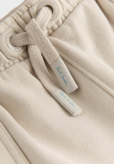 Ljust beige drawstring shorts tillverkade av mjukt tyg, med metallöglor och två synliga etiketter med "Paul Smith" i blått typsnitt.