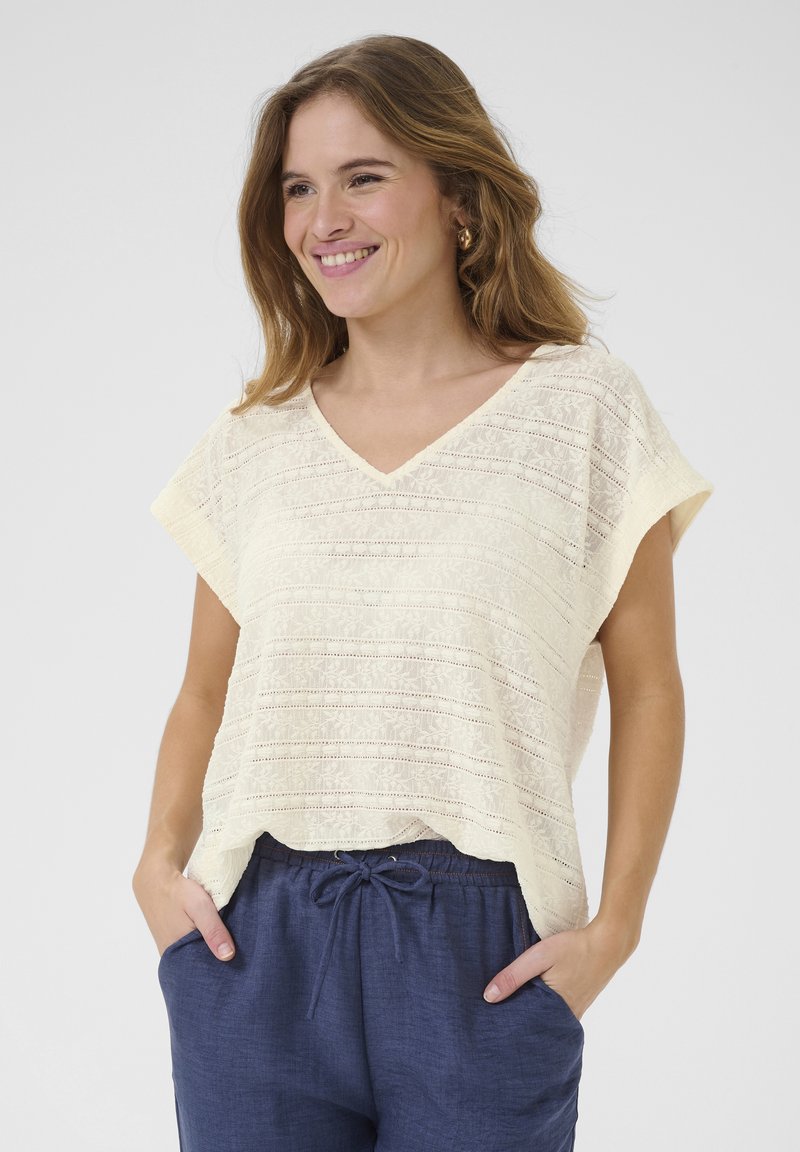 Top giallo chiaro a maniche corte con scollo a V, caratterizzato da una trama a strisce testurizzate; indossato con pantaloni blu scuro con coulisse.