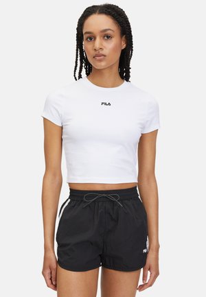 Witte crop-top t-shirt met korte mouwen en zwart "FILA" logo. Gecombineerd met zwarte shorts met een elastische tailleband en trekkoord.