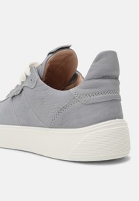 Sneaker in pelle grigia con finitura testurizzata, suola in gomma bianca a contrasto e punta arrotondata. Presenta lacci bianchi piatti e dettagli cuciti.