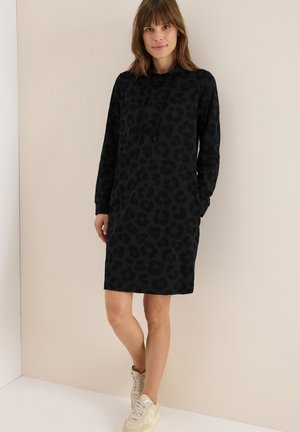 Svart hoodieklänning med en texturerad leopardtryck, med långa ärmar, avslappnad passform och sidofickor, upp tillsammans med ljusa sneakers.