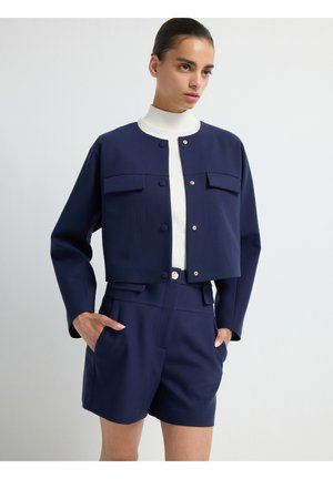 Marineblau verkürzte Jacke mit goldenen Knopfdetails und zwei Brusttaschen, kombiniert mit hoch taillierten Shorts aus demselben Material und derselben Farbe.