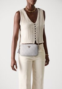 Graue, strukturierte Leder-Crossbody-Tasche mit silberner Kettenriemen und Logo. Trägt man zusammen mit einer crèmefarbenen Strickweste und hellen Hosen.