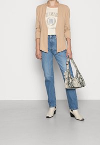 Beige blazer över en creamfärgad T-shirt med tryck, ljusblå jeans, vita ankelboots med svarta spetsar och en texturerad handväska i ormskinn.