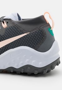 Baskets grises texturées avec une tige en mesh, des accents roses et une semelle extérieure blanche munie de crampons en caoutchouc pour la traction. Comprend une languette de tirage rose clair.