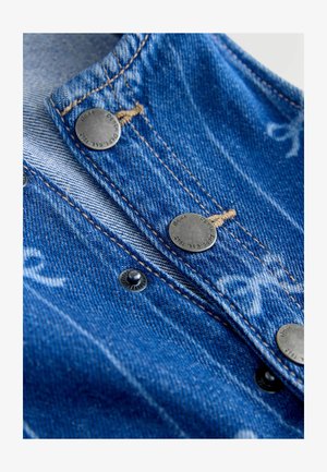 Close-up van blauwe denimstof met metalen drukknopen en beige stiksels, waarbij de textuur en de details van de knopen zichtbaar zijn.