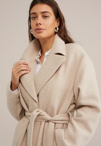 Beige, överdimensionerad ylleblandad kappa med en stor krage, bälte i midjan och mjuk textur. Har en vid silhuett och rena linjer.